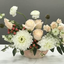 Blush roses and white blooms arranged in a low pink bowl