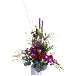 Tall arrangement of red roses, purple orchids, and lilies in a white vase