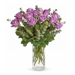 Purple roses in a clear glass vase with eucalyptus