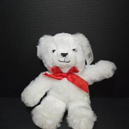 White teddy bear with a red ribbon bow on a black background