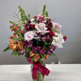 Mixed pink, white, and orange flowers arranged in a glass vase with a ribbon.
