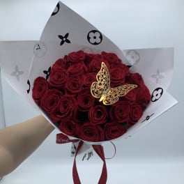 Bouquet of red roses wrapped in white paper with a gold butterfly accent