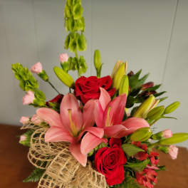 Bouquet of pink lilies and red roses with green filler in burlap wrap