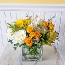 Yellow and white flower arrangement in a square glass vase