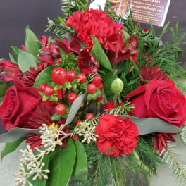 Red roses and carnations with berries in a square glass vase with a florist card