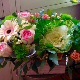 Mixed bouquet of pink roses, a gerbera daisy, and ornamental cabbage in a wooden box