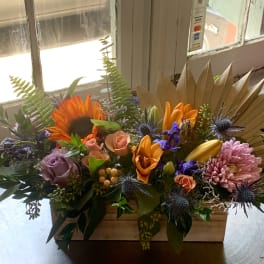 Mixed floral arrangement in a wooden box with sunflowers, roses, and lilies