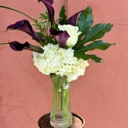 White hydrangeas and purple calla lilies in a clear glass vase