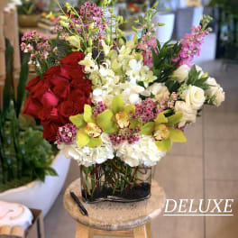 Mixed bouquet of red roses, white orchids, and pink flowers in a glass vase