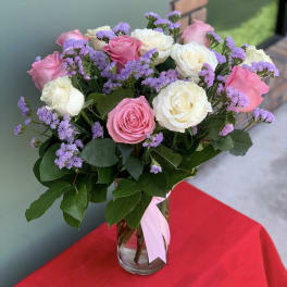 Pink and white roses with purple filler in a clear glass vase