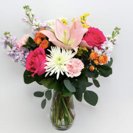 Mixed bouquet of pink, white, orange, and lavender flowers in a glass vase