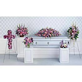 Pink and purple funeral floral arrangements around a silver casket