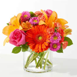 Bright mixed bouquet in a clear glass vase with pink, orange, and yellow blooms