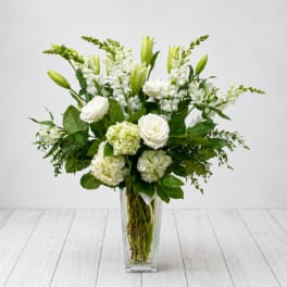 White flowers arranged in a clear glass vase with green accents