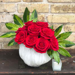 Red roses arranged in a white pumpkin-shaped vase with variegated leaves