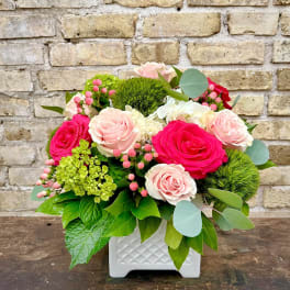 Pink and white roses in a white square vase with greenery