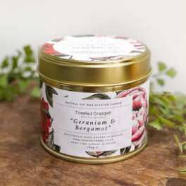 Gold tin candle jar with floral label on a wooden surface