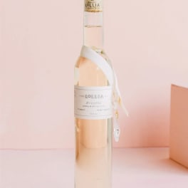 A tall clear bottle of Lollia bath oil with a ribbon tag