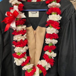 Red and white carnation lei draped over a black graduation gown