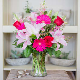 Pink lilies, hot pink gerbera daisies, and red roses in a clear glass vase