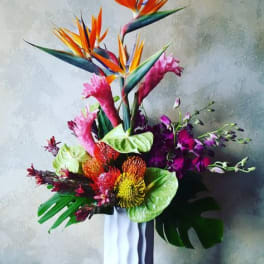 Tall tropical bouquet with orange bird-of-paradise and pink blooms in a white vase