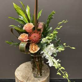 Tropical floral arrangement in a glass vase with peach roses and white orchids