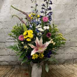 Tall mixed flower arrangement in a glass vase with a striped ribbon