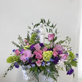 Pink and purple floral arrangement in a white pedestal urn with a statue