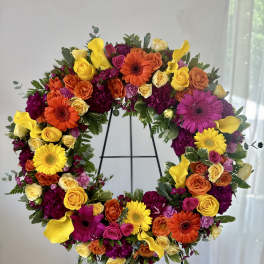 Large circular floral wreath on a stand with yellow, orange, pink, and purple blooms