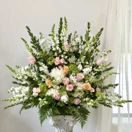 Large floral arrangement with pink and peach roses, white blooms, and greenery in a pedestal vase