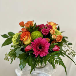 Bright mixed bouquet with pink gerbera, roses, and green mums in a glass vase