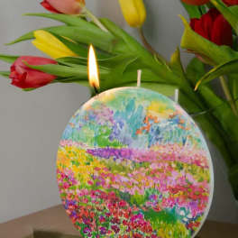 Tulips behind a colorful round candle with a lit wick