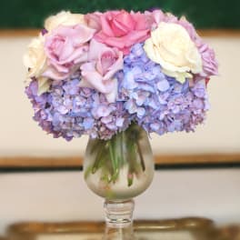 Pink and white roses arranged with lavender hydrangeas in a glass vase