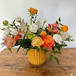Mixed bouquet of orange, white, and pink flowers in a yellow vase