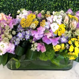 Mixed bouquet of purple, pink, white, and yellow flowers in a low rectangular vase