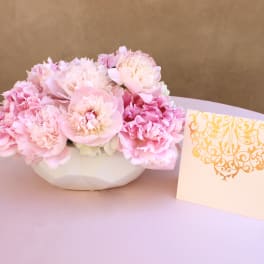 Pink peonies in a white bowl with a decorative card beside them
