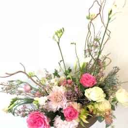 Pink and cream floral arrangement with tall branches in a low container