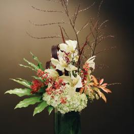 Tall floral arrangement with white orchids and red accents in a green glass vase