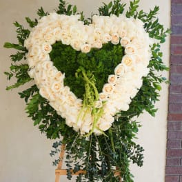 Heart-shaped white rose wreath on an easel with green foliage