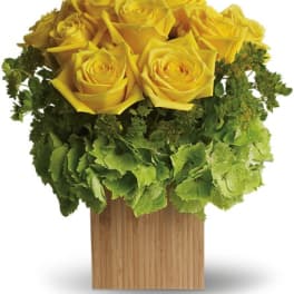 Yellow roses arranged in a wooden cube vase with green hydrangea