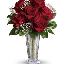 Red roses arranged in a tall silver vase with white filler flowers