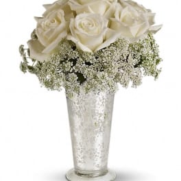 White roses in a tall clear vase with baby's breath