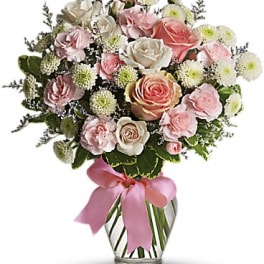 Pink and white rose bouquet in a clear glass vase with a pink ribbon