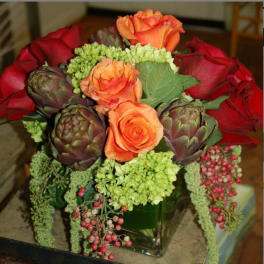 Bouquet of orange and red roses with artichokes in a glass vase