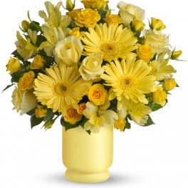 Yellow gerbera daisies, roses, and alstroemeria arranged tightly in a soft yellow vase