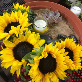 Sunflowers arranged around candles and a small succulent in a shallow planter