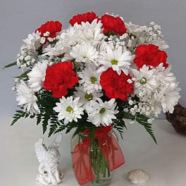 Red carnations and white daisies in a glass vase with a red ribbon