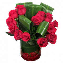 Red roses arranged in a clear vase with broad green leaves