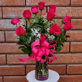 Pink roses arranged in a clear glass vase with a bright pink bow.