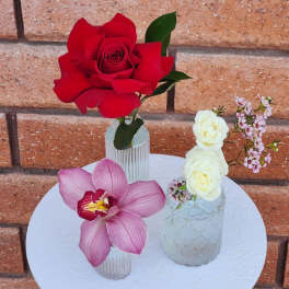 Three small floral arrangements with roses and orchids on a white table.